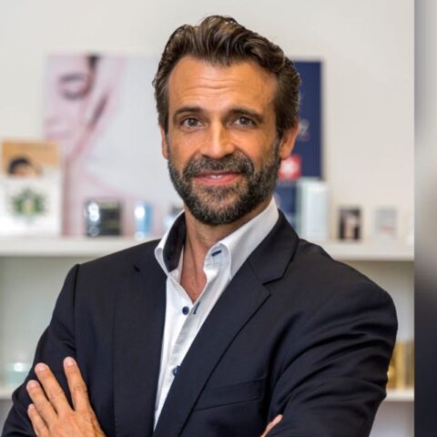 Porträt eines Geschäftsführer Stefan Neider im dunklen Anzug, lächelnd vor einem Regal in Büro- oder Praxisumgebung